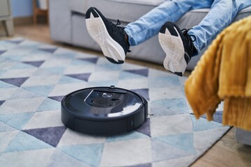 African american man cleaning rug using robot vacuum cleaner at home