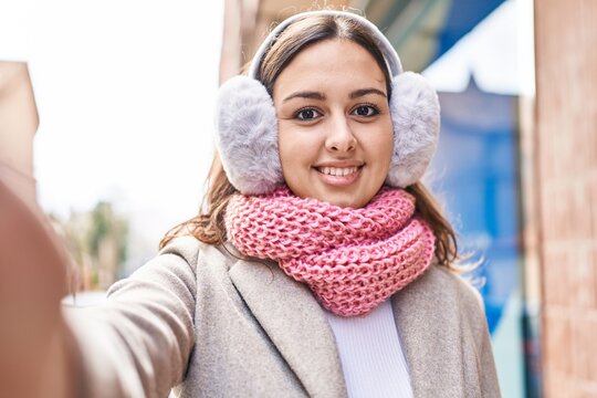 Young beautiful hispanic woman make selfie by camera wearing scarf and earmuff at street