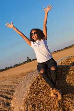 A beautiful, happy mixed race African American female girl child teenager young woman celebrating arms raised in sunshine wearing sunglasses and smiling with perfect teeth