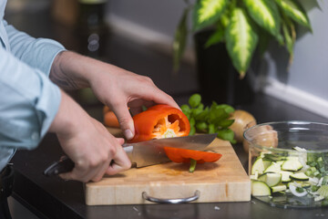 cutting red pepper into slices preparing food on wooden cutting board.
