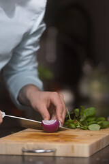 Chef cutting red onion down the middle, prepairing healthy food on a wooden cutting board.
