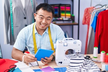 Young chinese man tailor smiling confident using touchpad at tailor shop