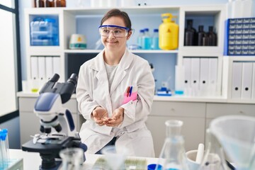 Fototapeta premium Hispanic girl with down syndrome working at scientist laboratory with hands together and crossed fingers smiling relaxed and cheerful. success and optimistic
