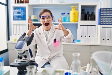 Hispanic girl with down syndrome working at scientist laboratory shouting frustrated with rage, hands trying to strangle, yelling mad