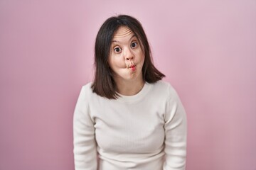 Fototapeta premium Woman with down syndrome standing over pink background making fish face with lips, crazy and comical gesture. funny expression.