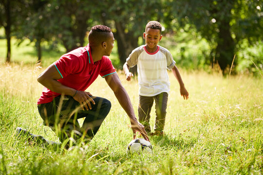 Happy black people doing sport practice in city park. African american family with father teaching son how to play football.