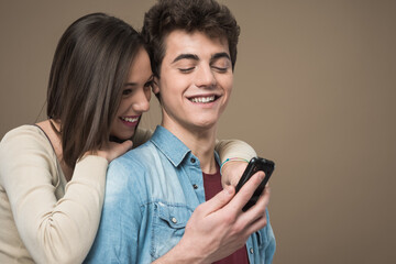 Fototapeta premium Cheerful young teen smiling couple with mobile phone enjoying together