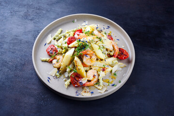 White asparagus glazed with fried king prawns and pistachio pasta served as close-up on a design plate with text space