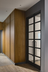 Glowing hall in a modern style with gray walls and tiles with a parquet on the floor. There is a large wooden wardrobe, gray door and glass black door. Vertical.