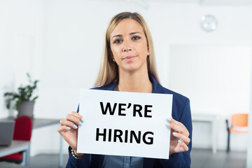business woman in a workplace holding a hiring sign as an invitation