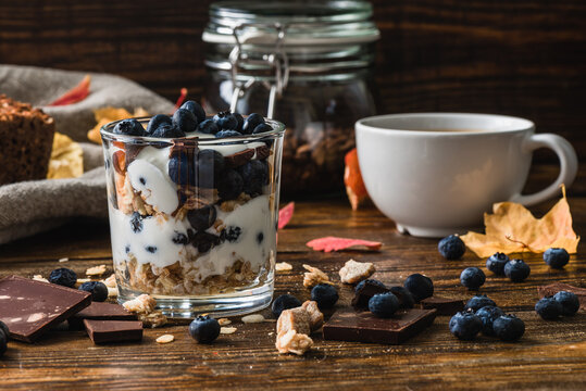 Granola with yogurt, blueberries, honey and chocolate bars. And cup of coffee on backdrop.