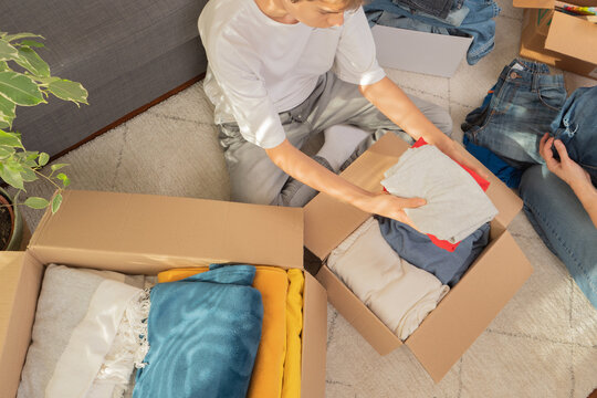 Mother and son sorting clothes and packing into cardboard box. Donations for charity, help low income families, declutter home, sell online, moving moving into new home, recycling, sustainable living