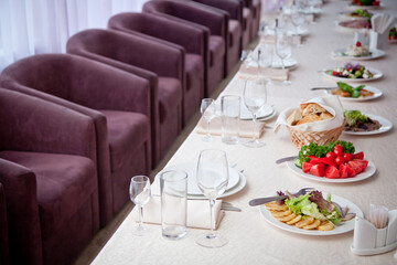 a table covered with a white tablecloth with salads, glasses, plates, napkins and a number of seats