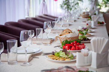 a table covered with a white tablecloth with salads, glasses, plates, napkins and a number of seats