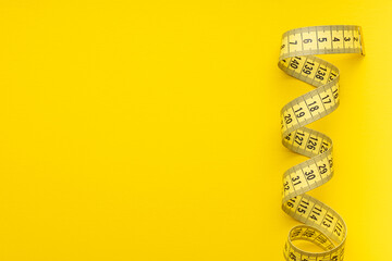 Yellow measuring tape on yellow background. Top view.
