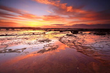 Fototapeta na wymiar Sunrise skies reflecting on the exposed rock shelf at Long Reef, Northern Beaches, Australia