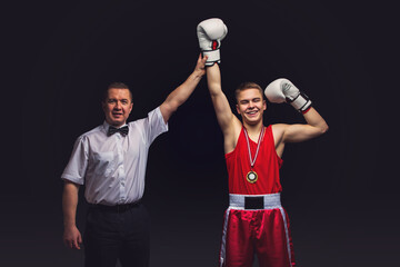 Boxing referee gives medal to young teen boxer in red form and white gloves. Winner. Studio shot on...