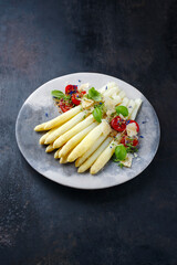 White asparagus glazed with cherry tomatoes and parmesan cheese served as close-up on a design plate with text space