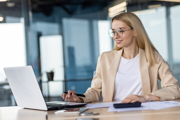 Portrait of smiling young business woman, bank employee, manager working in office with documents and laptop