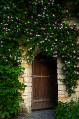 Fototapeta na wymiar Zabytkowe mury i wejście do klasztoru przez drewniane zdobione drzwi. Kolorowe kwiaty na zabytkowym murze. 