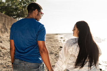 Young biracial couple holding hands at beach sunset.