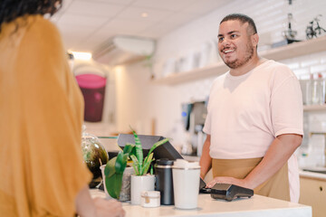 Latin man serving a customer using a computer at a coffee shop in Brazil