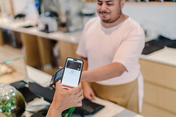 Latin attendant receiving proximity payment with smartphone in a coffee shop in Brazil