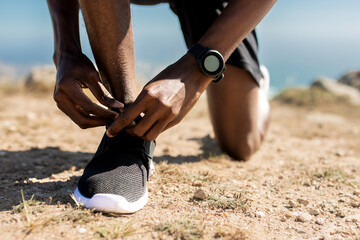 Training, healthy lifestyle concept. Closeup view of unrecognizable black man tying his shoelaces before jogging outdoors - obrazy, fototapety, plakaty