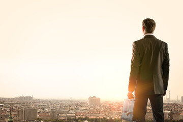 Businessman standing with back against morning city, panoramic view - Powered by Adobe