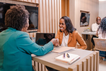 black Brazilian woman bank manager in Brazil shaking her client's hand after they sign a loan agreement - obrazy, fototapety, plakaty