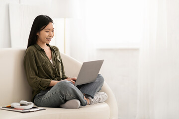 Fototapeta premium Smiling chinese woman sitting on couch with computer