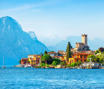 Ancient tower and fortress in old town Malcesine at Garda lake, Veneto region, Italy. High snowbound top mountains on background. Summer landscape with colorful houses and green trees.
