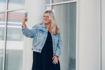 Urban portrait young woman plus size wearing denim texting on mobile phone.