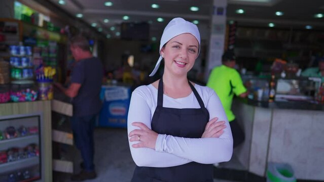 One joyful waitress smiling at camera with arms crossed with restaurant in background. Female server wearing uniform standing in front of small business, job Occupation concept