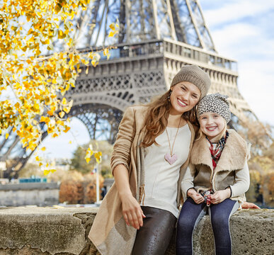 Autumn getaways in Paris with family. Portrait of happy mother and child tourists on embankment in Paris, France sitting on the parapet