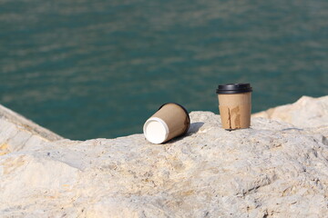 Disposable cardboard cup with plastic lid thrown on the floor. Dirty coffee cup on floor in Mediterranean Sea port. World Environment Day concept idea. Selective focus on disposable cardboard cup. 
