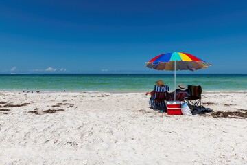 Fototapeta na wymiar Beautiful sandy beach with colorful umbrella and beach chairs in tropical beach park in Naples, Florida