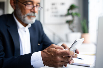 Serious mature european man in suit chatting on phone, use app for check account in office...