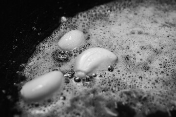 black and white classic photo, fried garlic cloves in a pan in oil, close-up view, top view