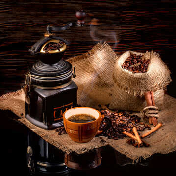 Cup of coffee, cinnamon sticks, star anise, a bag of roasted coffee beans on sackcloth stand on a glossy black surface, on a brown background