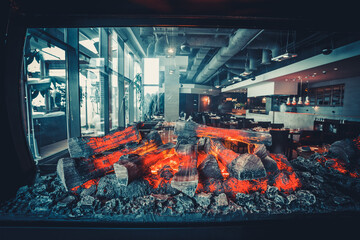Restaurant kitchen interior: brazier with burning wood, made of natural stone with fire for BBQ. In...