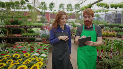 A male employee showing inventory to female colleague walking inside flower shop. Entrepreneurial concept of local store with staff using modern technology