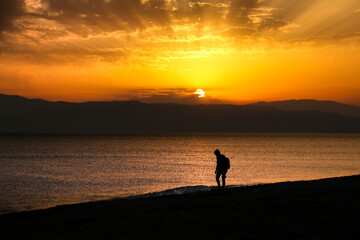 Woman walking by the shore at sunset