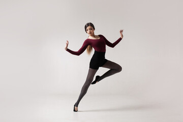 young beautiful woman dancer with long brown hair wearing maroon swimsuit posing on a light grey studio background