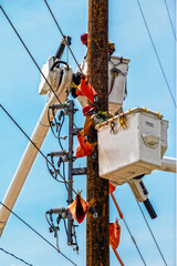 Two line workers electricians in buckets high in air repairing an electric pole after storm
