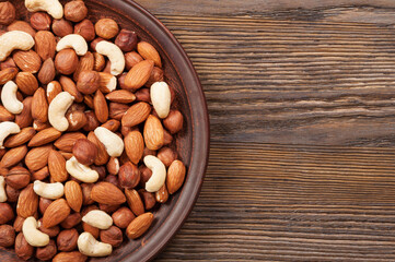 Different nuts in plate on a wooden background. Almond, hazelnut and cashew.