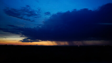 storm clouds at sunset with bursts of rain in the distance on the horizon and a line of reddish sky
