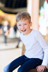 smiling positive boy sitting at outdoor shopping mall with other people in the background enjoying the time