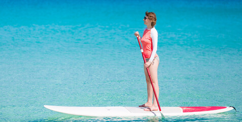 young woman enjoying stand up paddling, active and healthy summer vacation activity