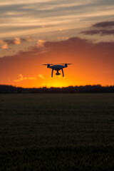 Drone silhouetted against orange sunset taking video